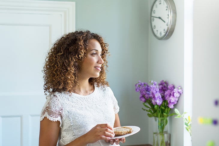 Intermittent Fasting Woman eating in the kitchen near a clock
