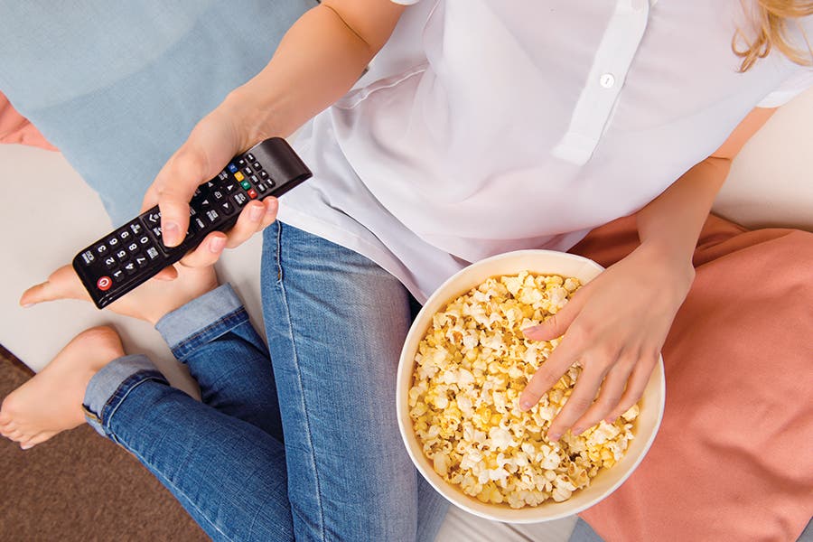 Habits That Age You Woman watching TV with popcorn getting older