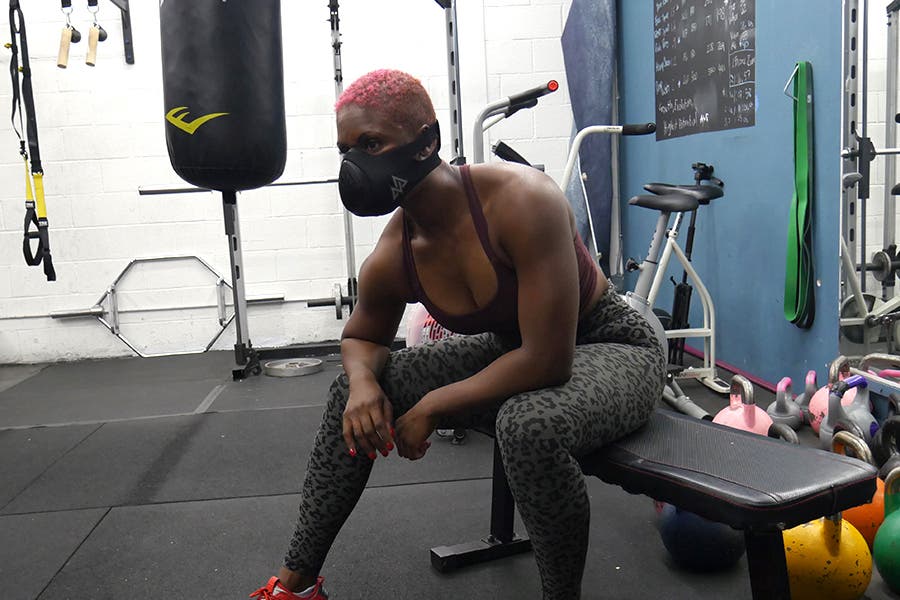 Woman sitting on exercise bench in gym with face mask on