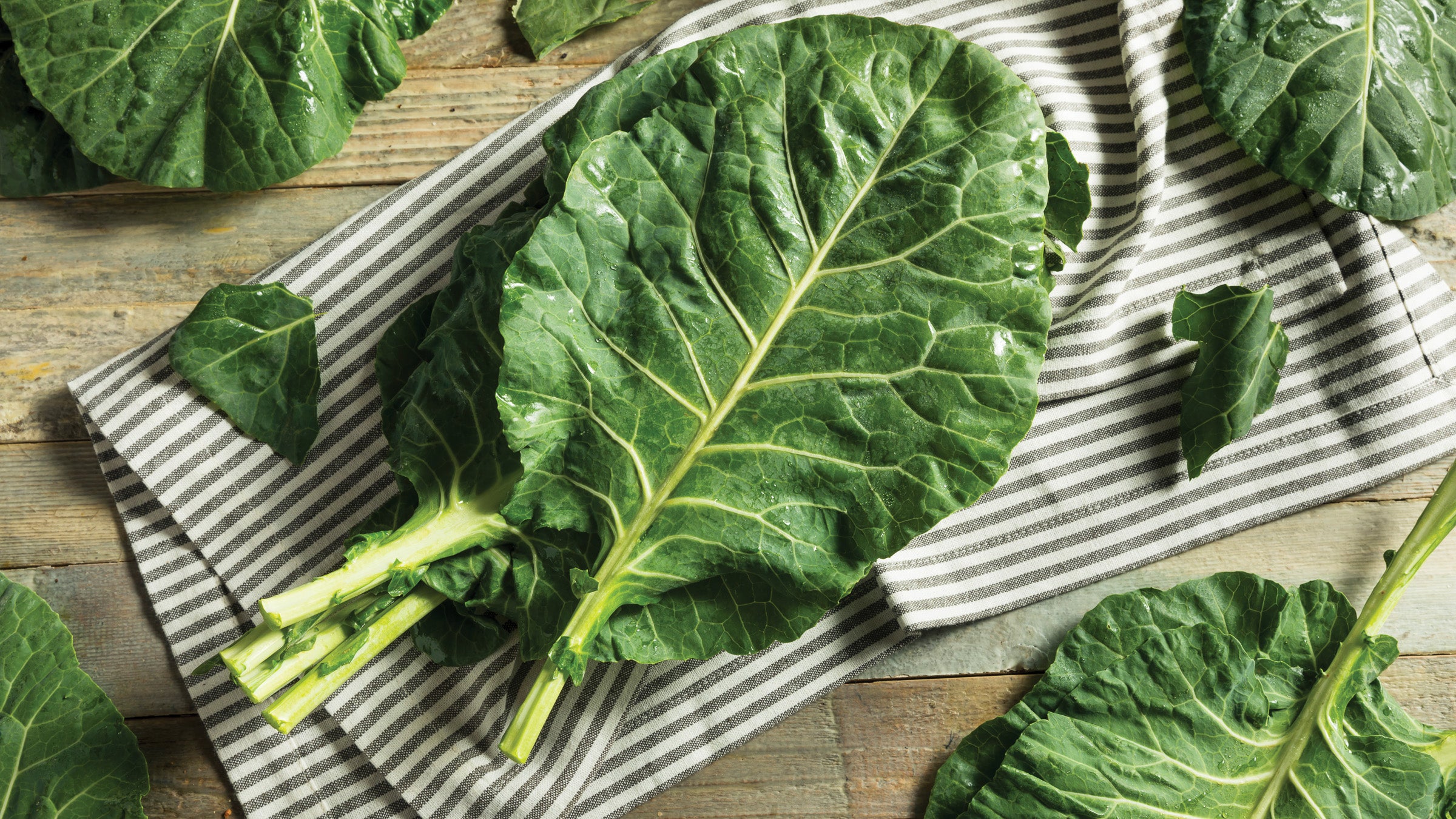 Leaves of raw green collards on a striped kitchen towel