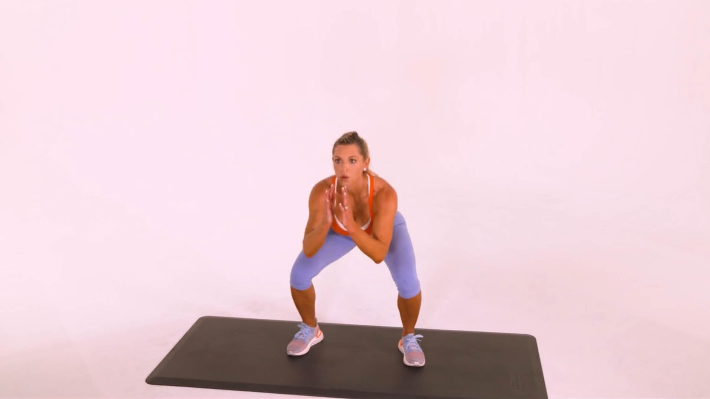 Woman performing an air squat on an exercise mat demonstrating proper form