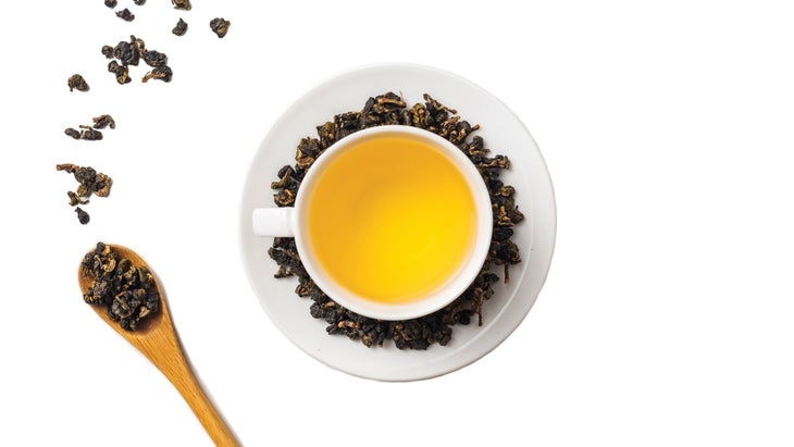 Oolong tea leaves in a wooden spoon and brewed in a cup