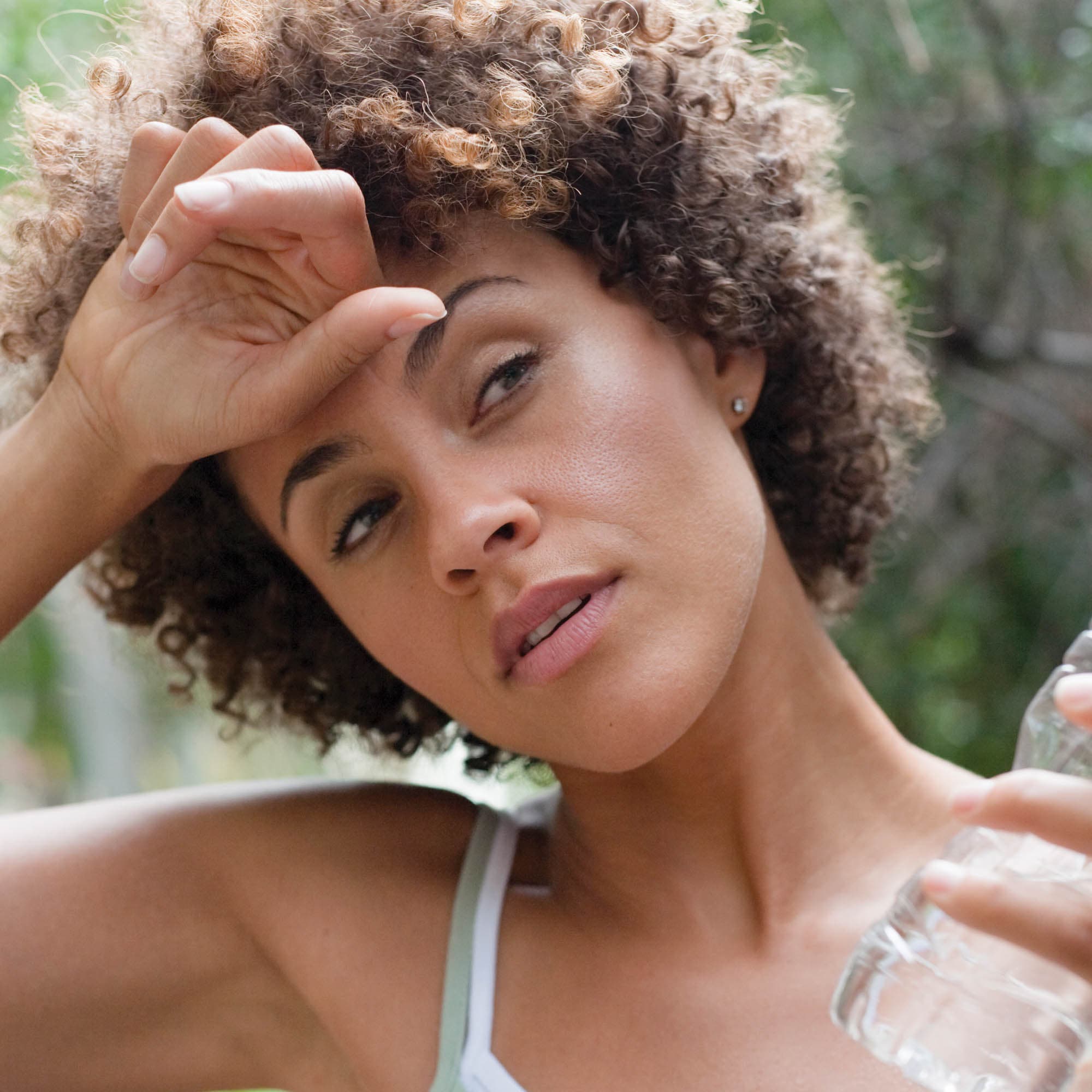 Woman holding a water bottle and wiping her forehead